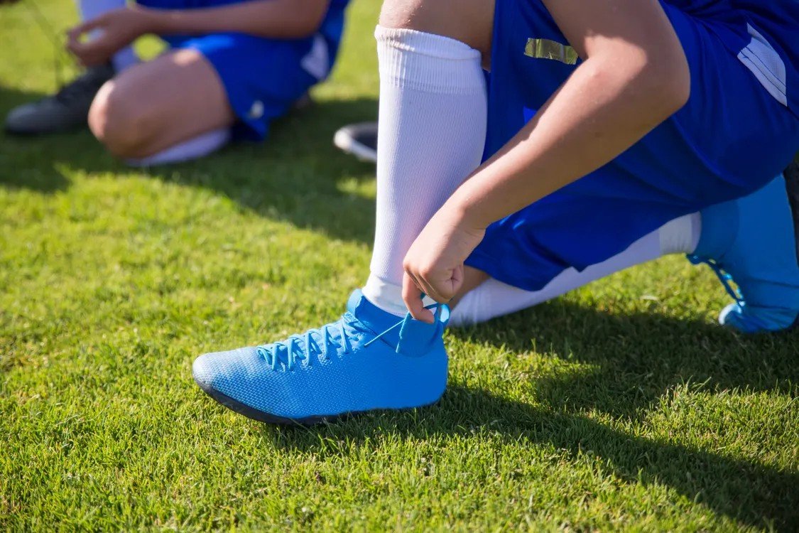 Footballer tying the laces of blue football boots on grass