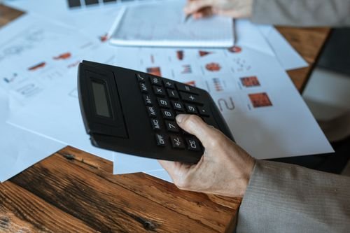 Hand using a calculator on a wooden desk with business charts