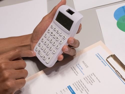 Hands using a calculator next to a business invoice