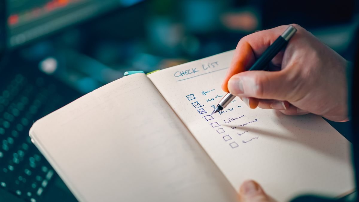 Hand writing on a paper checklist in a notebook to plan a client onboarding process