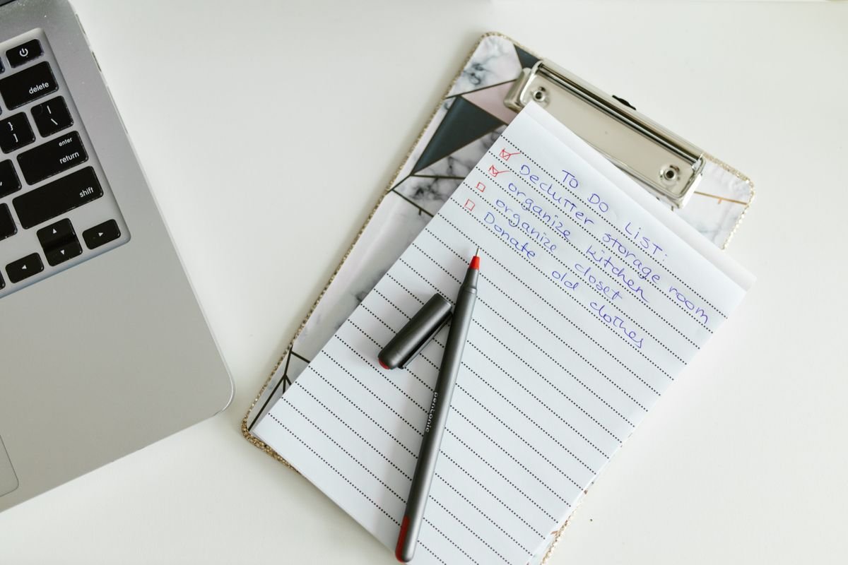 Organized to do list on a clipboard next to a laptop and pen on a desk
