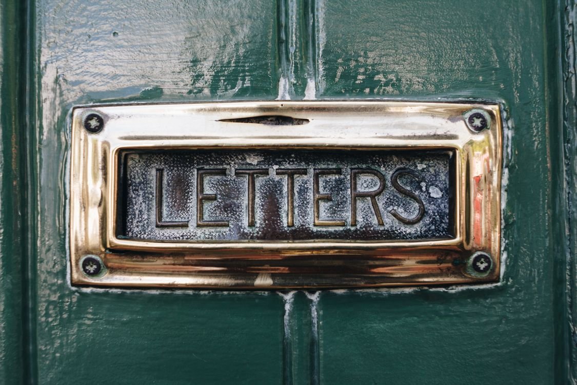 Brass mail slot with the word letters on a green door