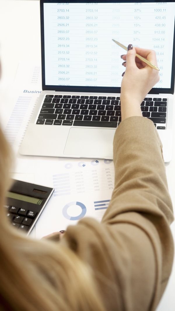 Woman pointing at spreadsheet numbers on a laptop with a calculator nearby