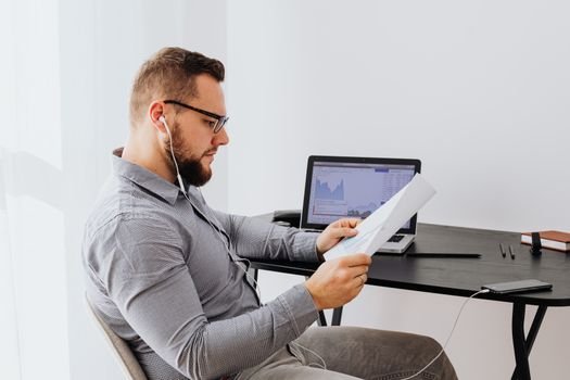 Man reviewing printed financial reports with a laptop on his desk