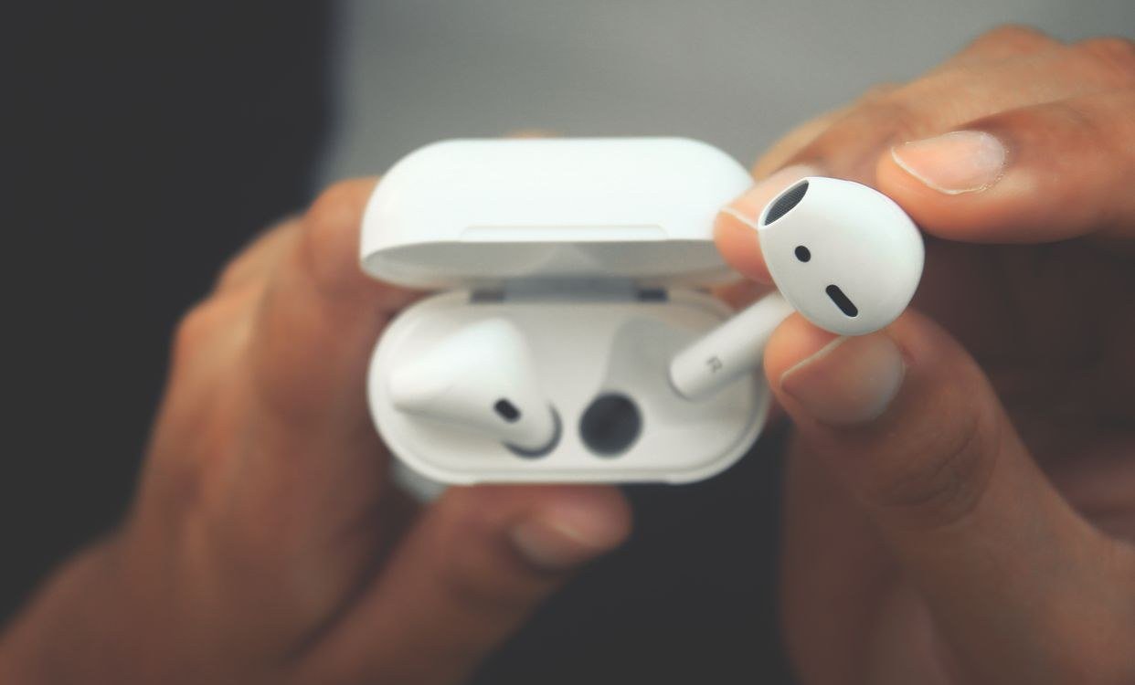 Hands holding wireless earbuds with an open charging case