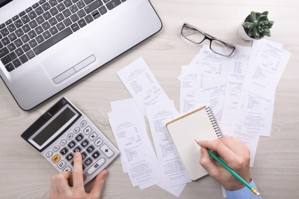 Freelancer tracking business expenses with calculator, receipts and laptop on a desk