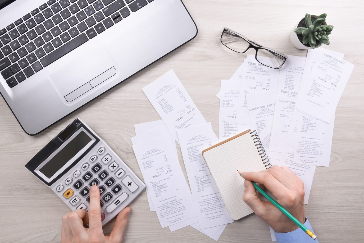 Freelancer tracking business expenses with calculator, receipts and laptop on a desk