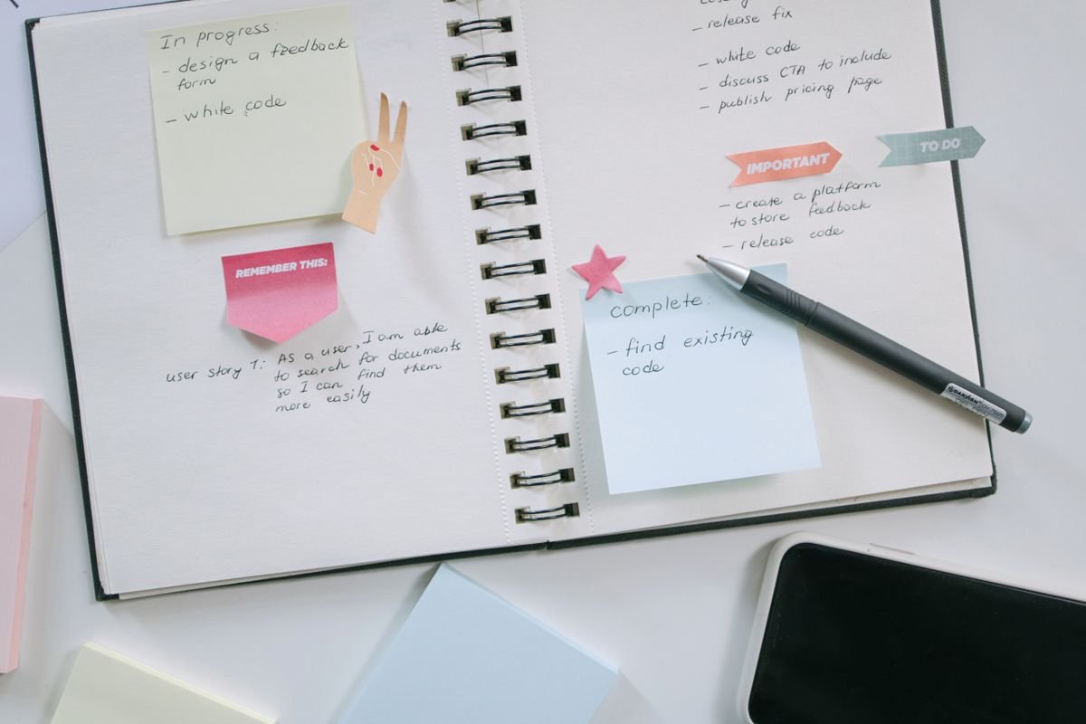 Open notebook with a weekly task plan, colorful sticky notes, and a pen on a white desk