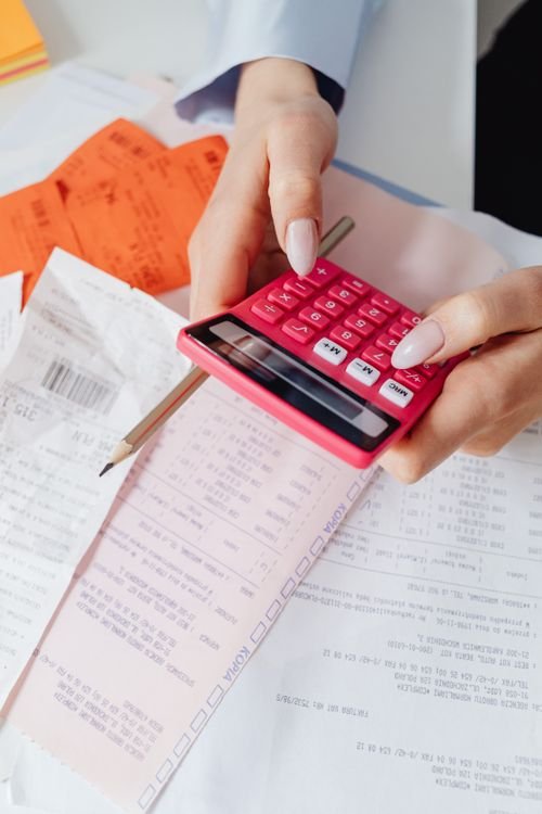 Small business owner using a calculator to review invoices and receipts before a customer credit check