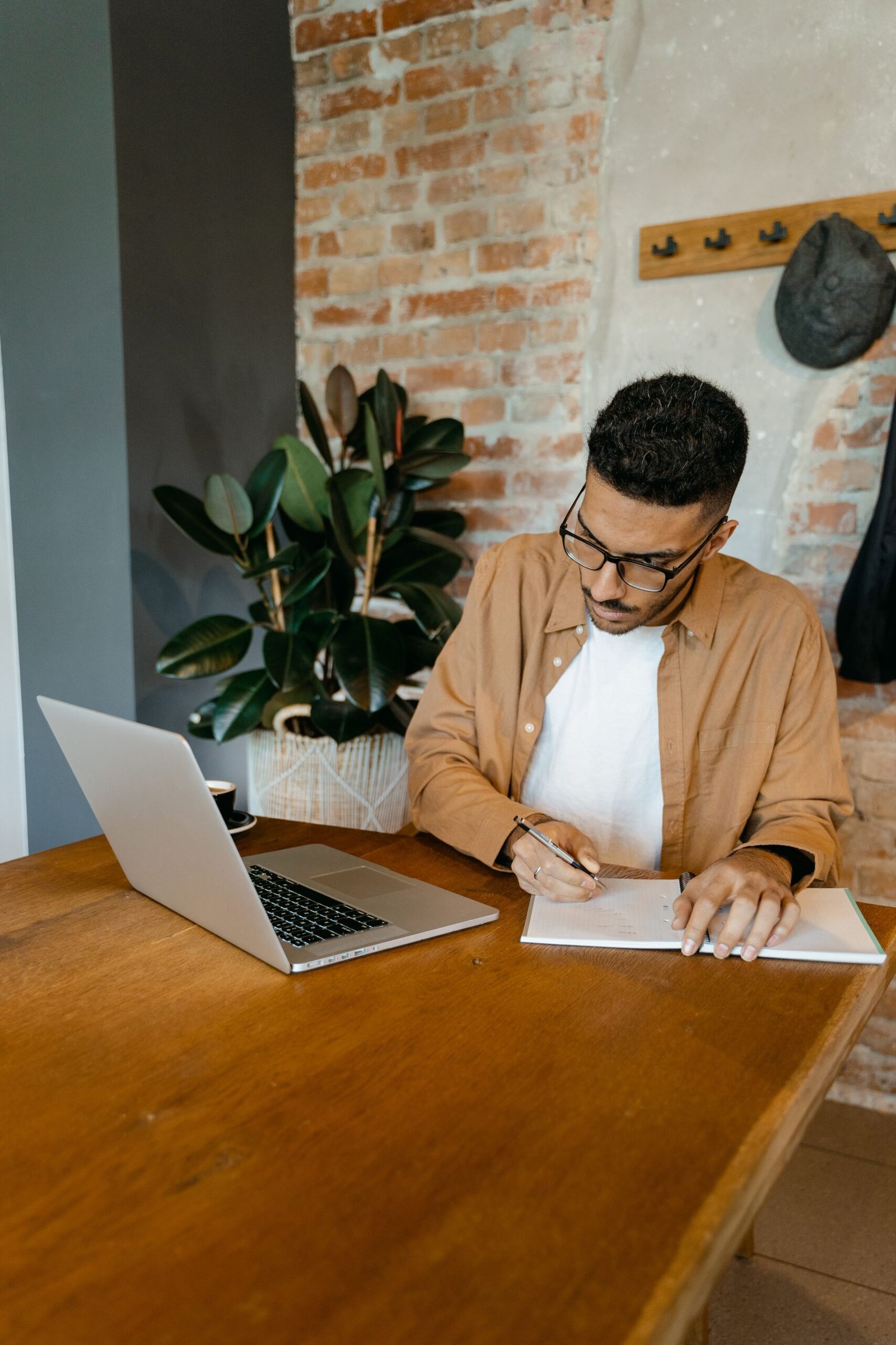 Man writing notes at a desk with a laptop open beside him.