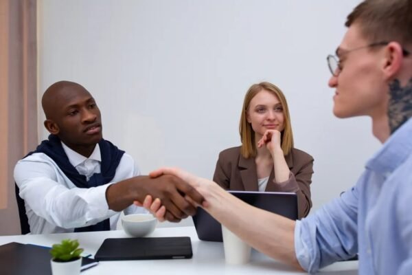 Two businessmen shaking hands across a meeting table while a colleague looks on