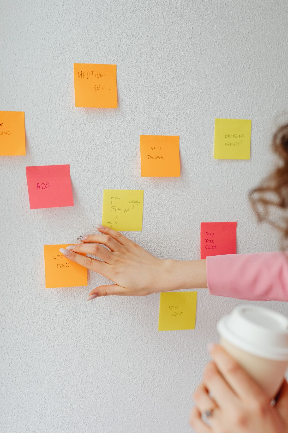 Hand placing colorful sticky notes labeled with marketing topics on a wall during a content brainstorm