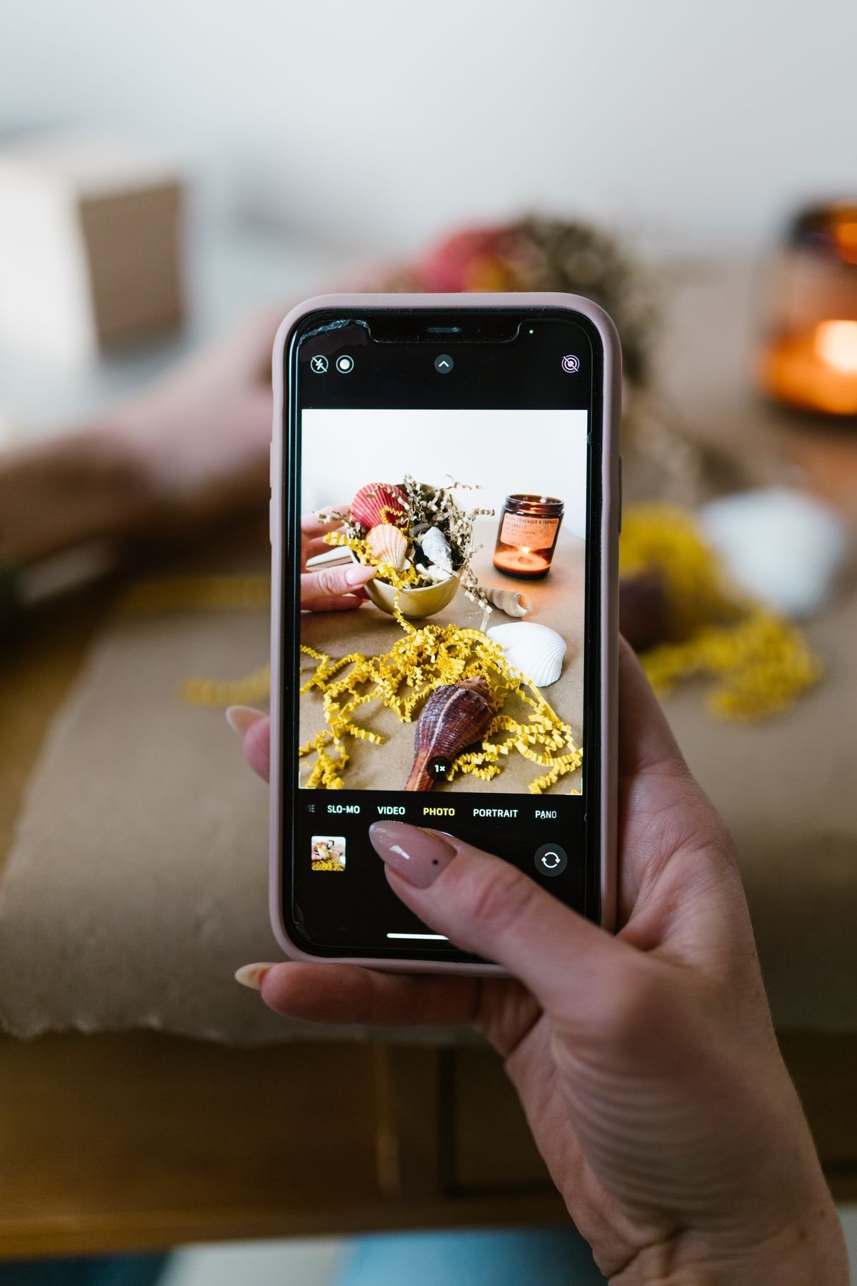 Hand holding a smartphone taking a photo of a styled product flat lay with a candle for content creation