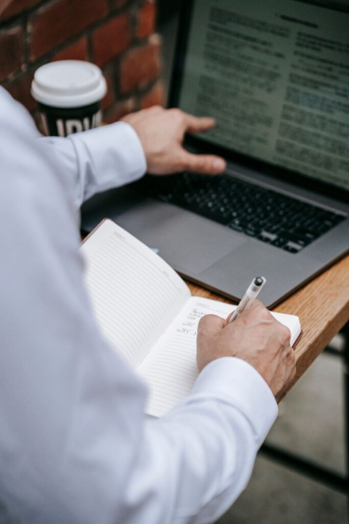 Person writing in a notebook beside a laptop while drafting a job advert