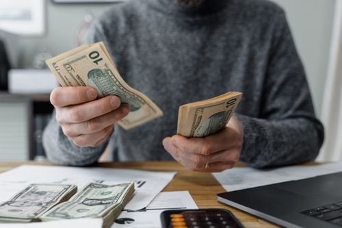 Shop worker counting cash notes at a desk with a calculator nearby