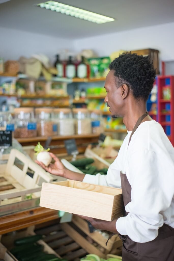 Shopkeeper holding a wooden crate of stock in a small shop