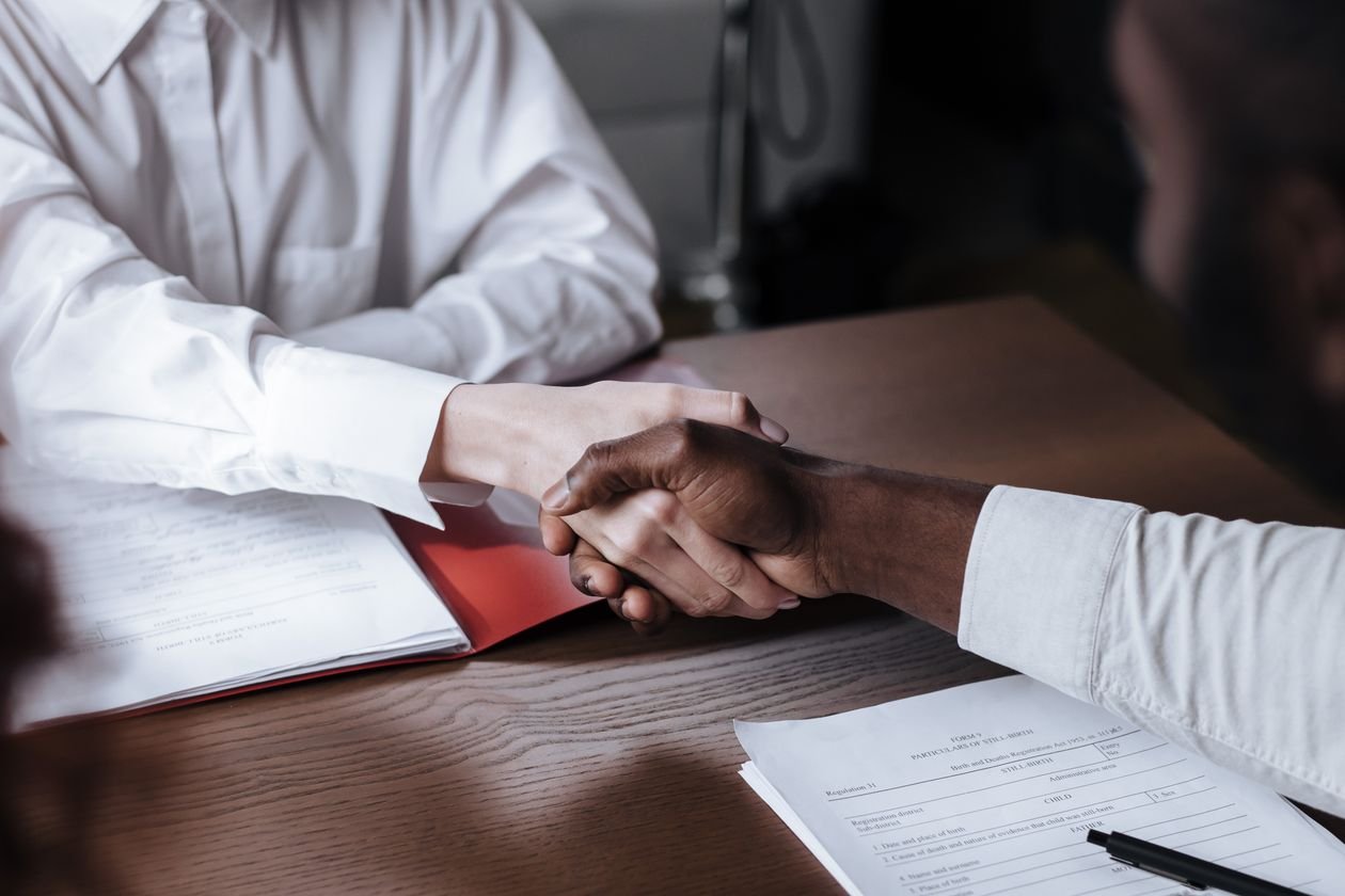 Two business partners shaking hands over contract documents on a wooden desk