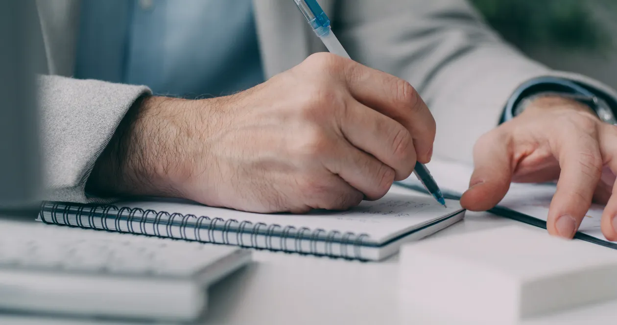 Hands writing notes in a notebook at a desk