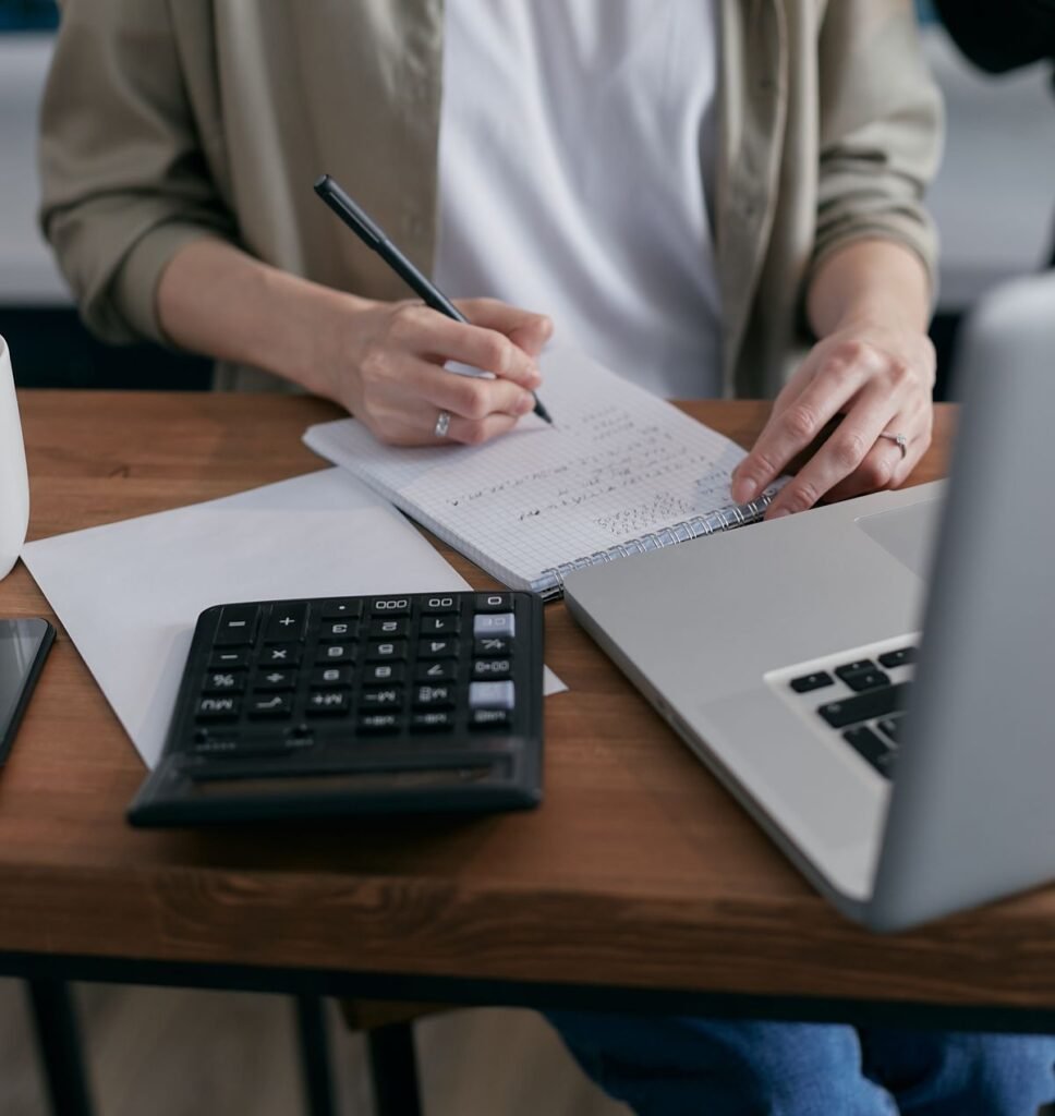 Woman writing financial calculations in a notebook with a calculator nearby