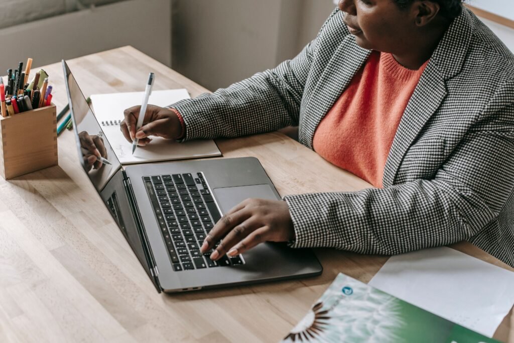 Professional woman typing on a laptop and writing notes at her desk