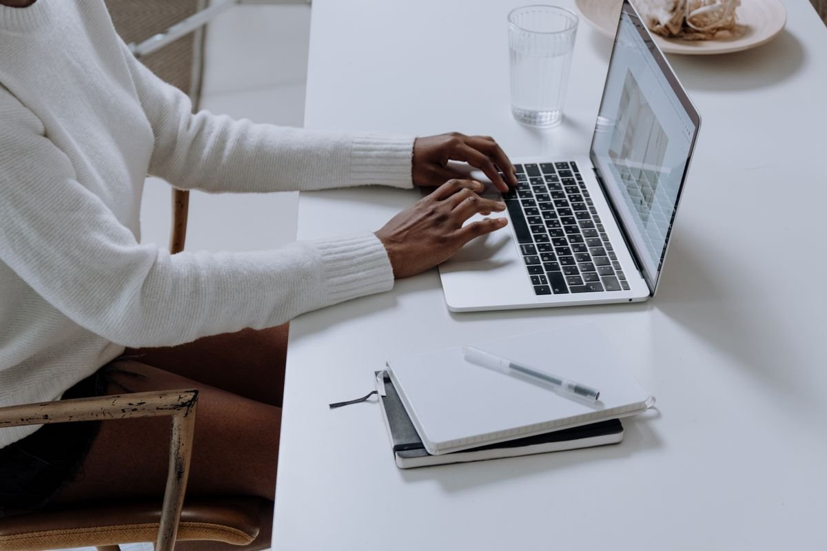 Person writing a business email in English at a white desk with a notebook and pen nearby