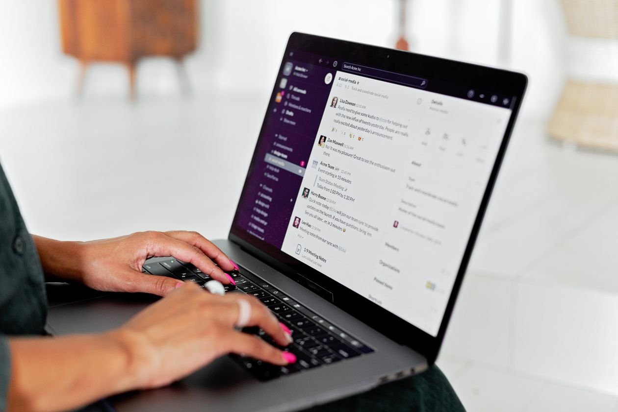 Woman typing a message on a laptop with a team chat app on the screen
