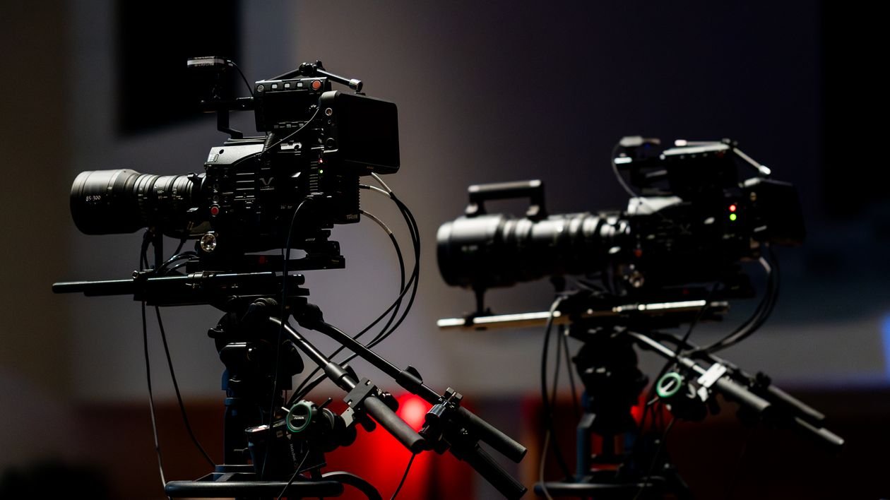 Two professional television cameras on tripods inside a dark studio