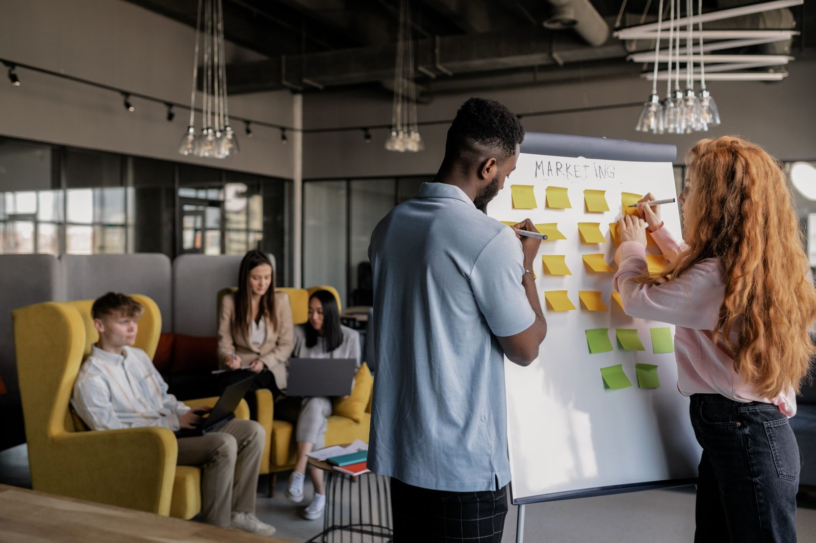 Two people writing sticky notes on a whiteboard