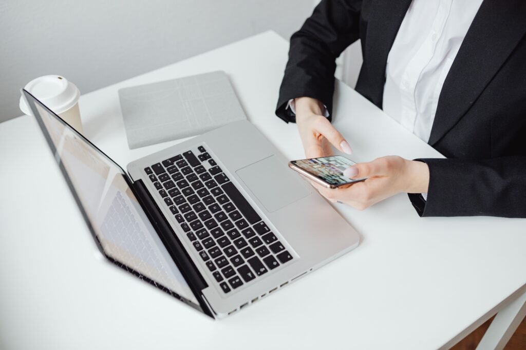Business person checking a smartphone with a laptop and coffee cup on the desk