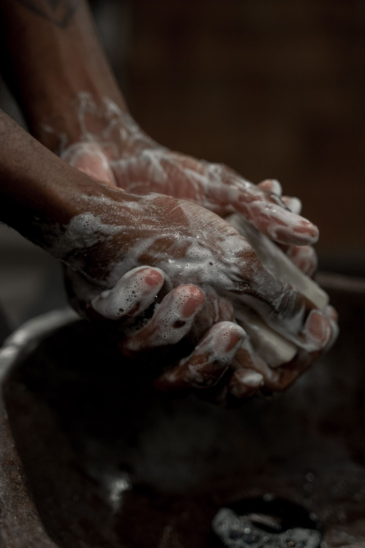 Hands covered in soap suds while hand washing in a basin