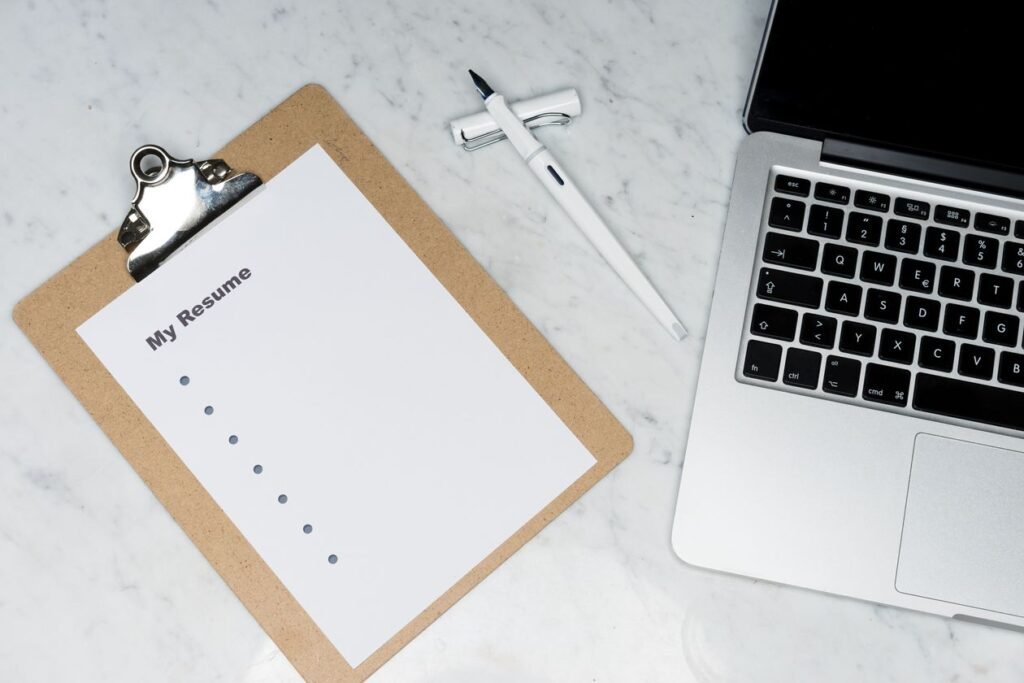 Resume on a clipboard beside a laptop during application review