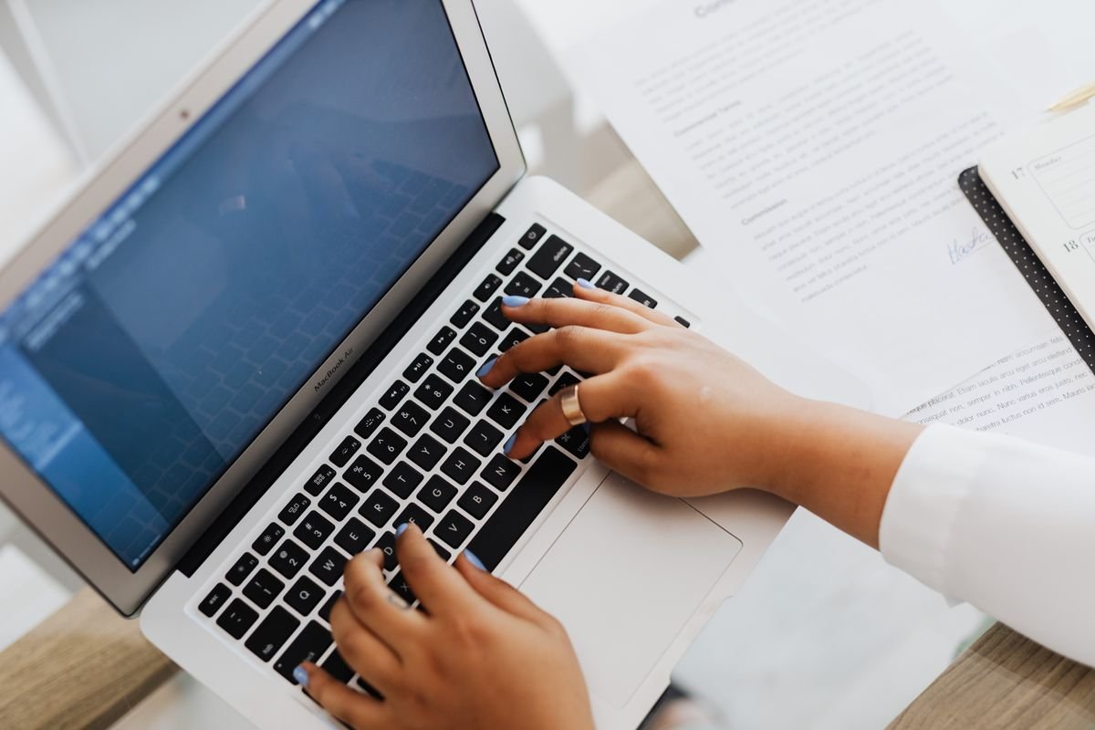 Hands typing a business email in English on a laptop beside a printed document
