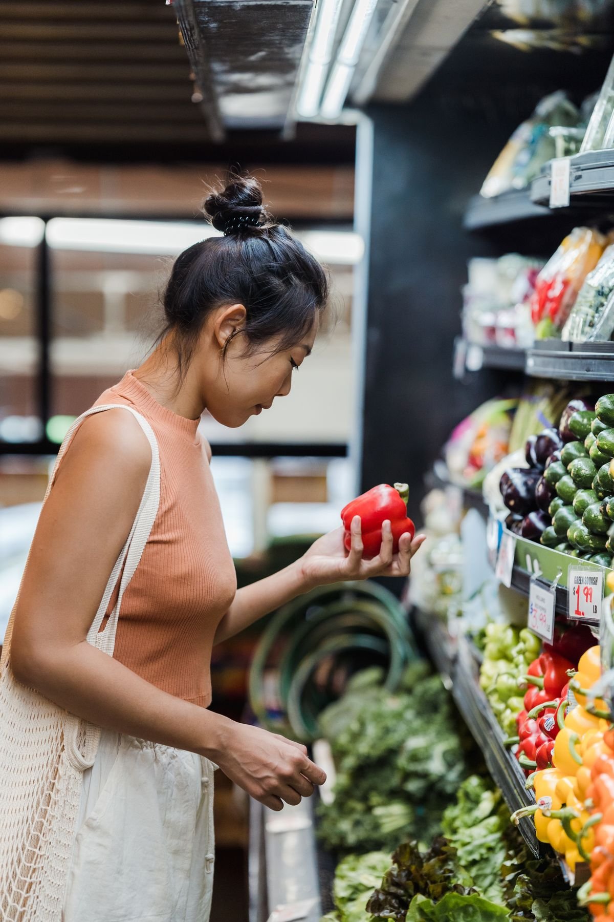 Woman examining a red bell pepper in a supermarket produce aisle