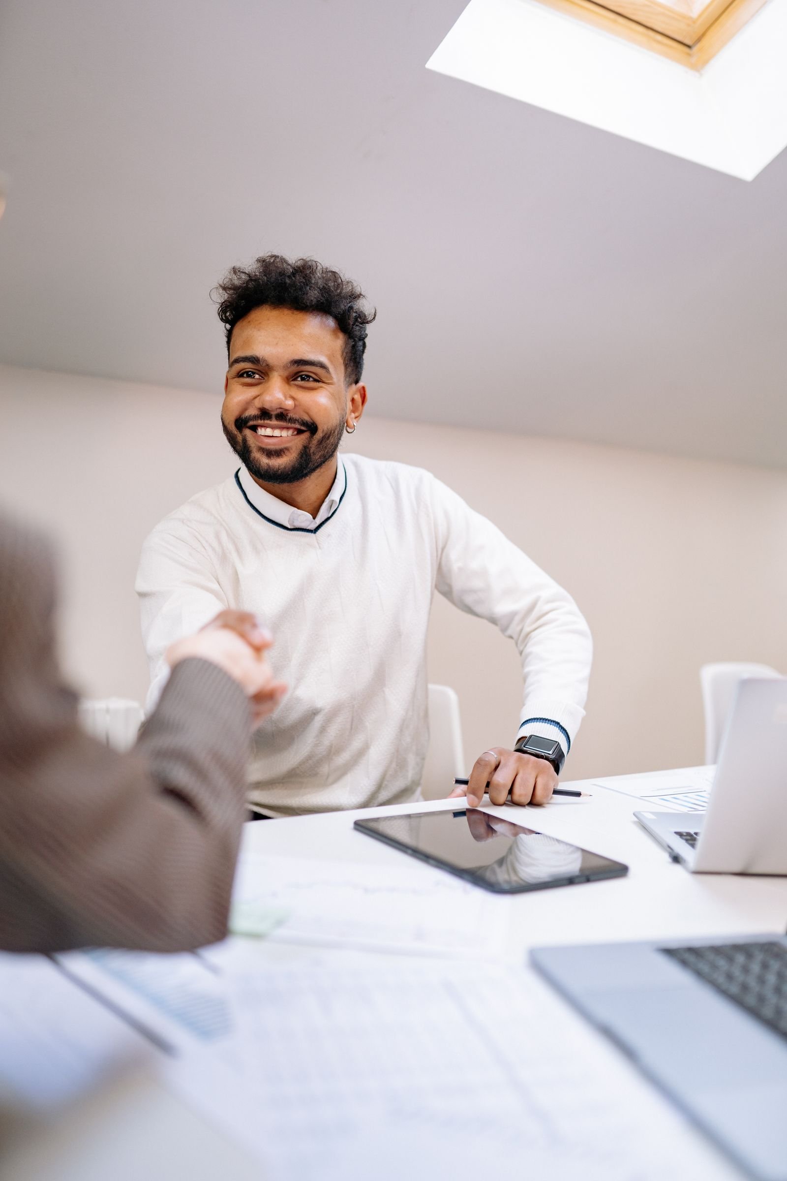 New hire shaking hands with an employer across a desk with a laptop