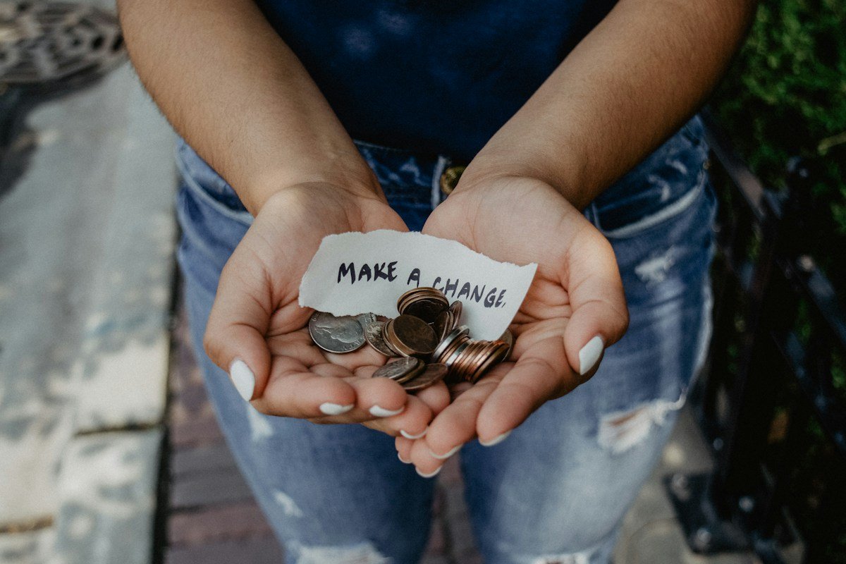 Cupped hands holding coins and a handwritten make a change note symbolising a charity donation