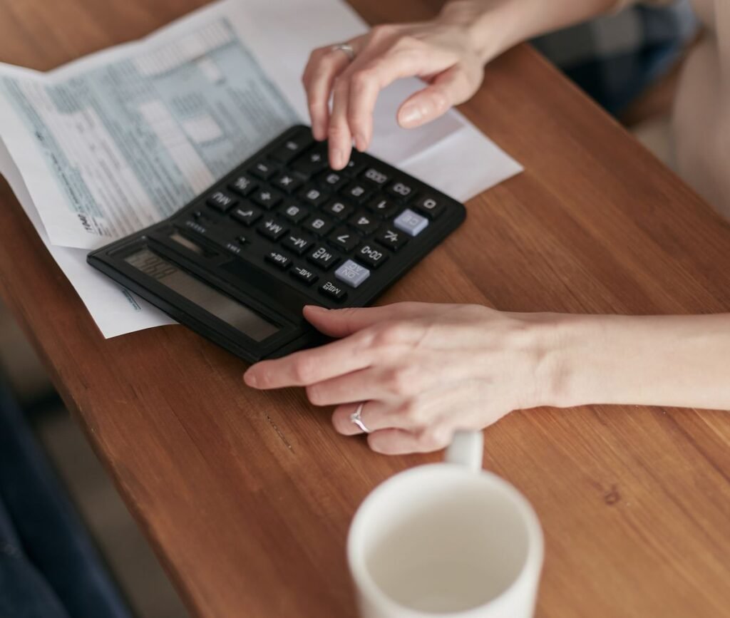 Hands using a calculator on top of invoice paperwork at a wooden desk