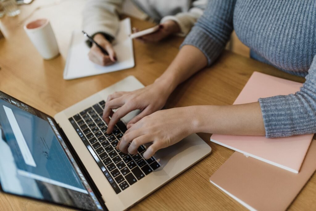 Freelancer typing on a laptop with coffee and notepad at a wooden desk