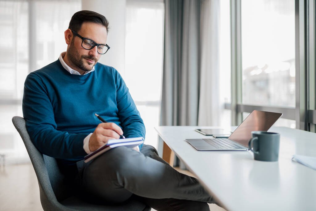Entrepreneur writing business plan notes in a notebook while working at a desk