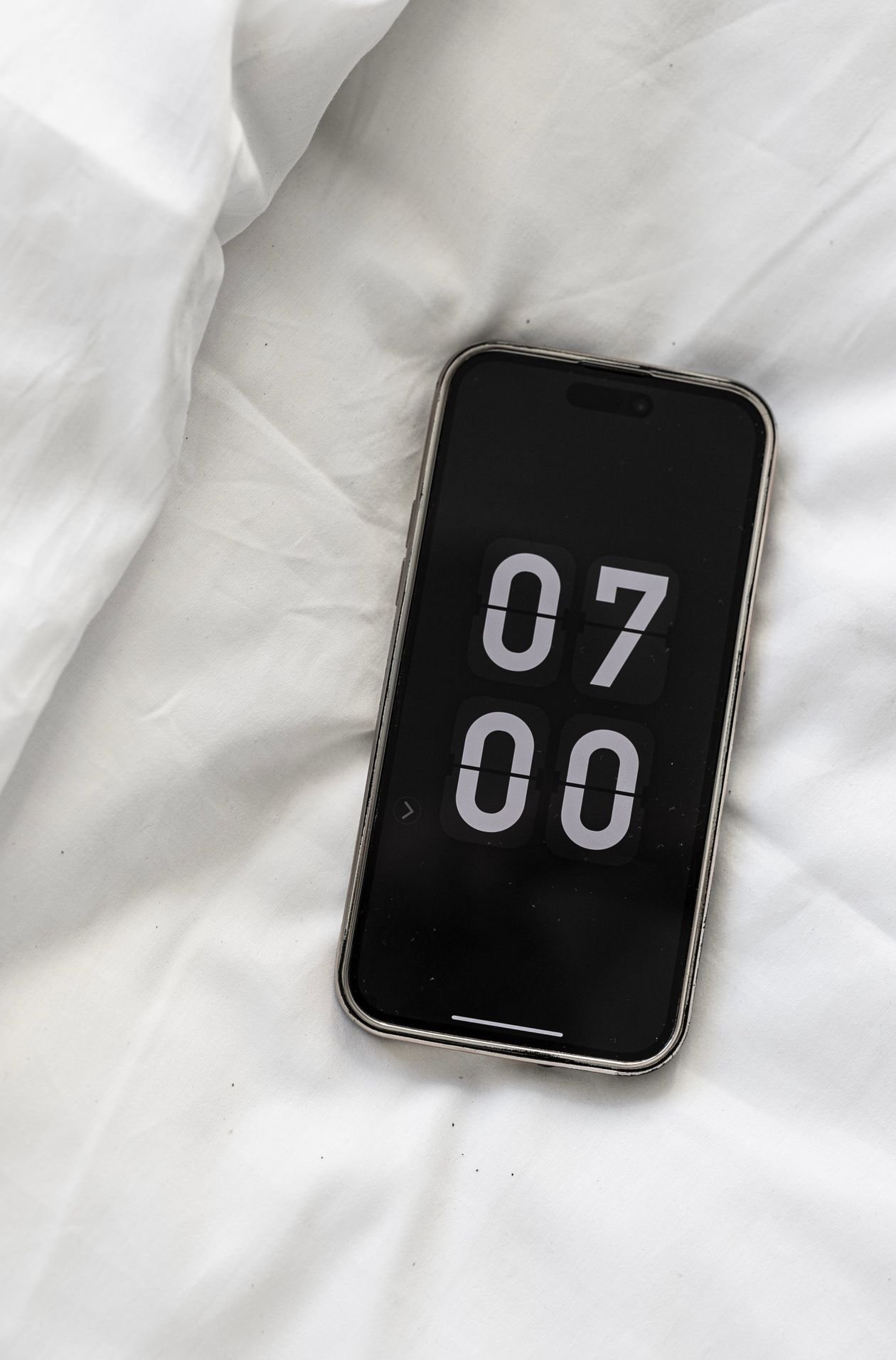 iPhone lying on a bed showing a seven o clock morning alarm